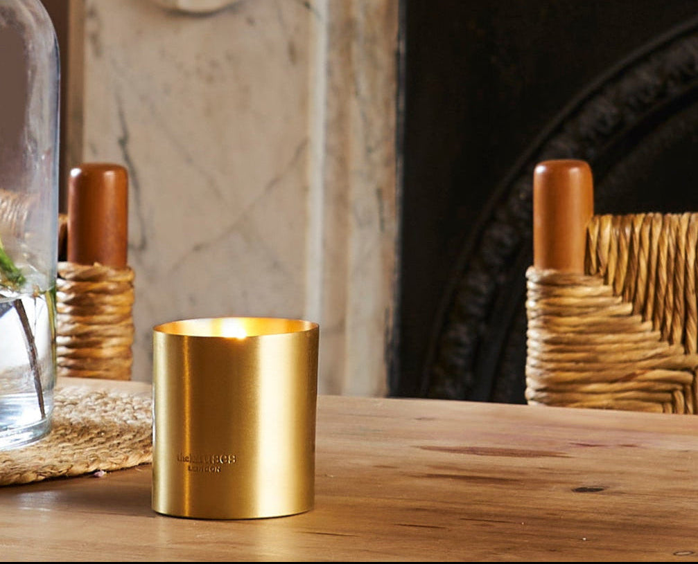 Gold candle on a wooden table with a fireplace and decorative items in the background