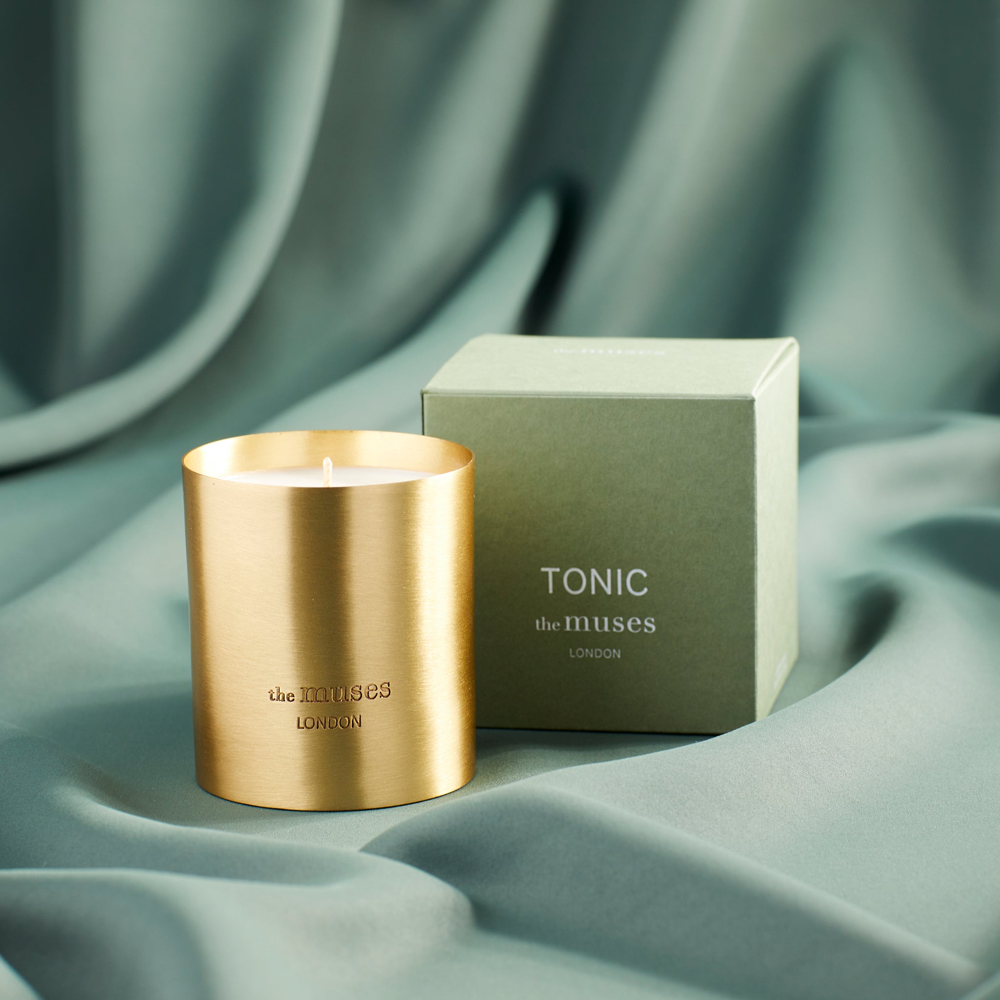 Tonic scented 100% natural wax candle 220g in pure brass container next to green candle box with closed lid. Front