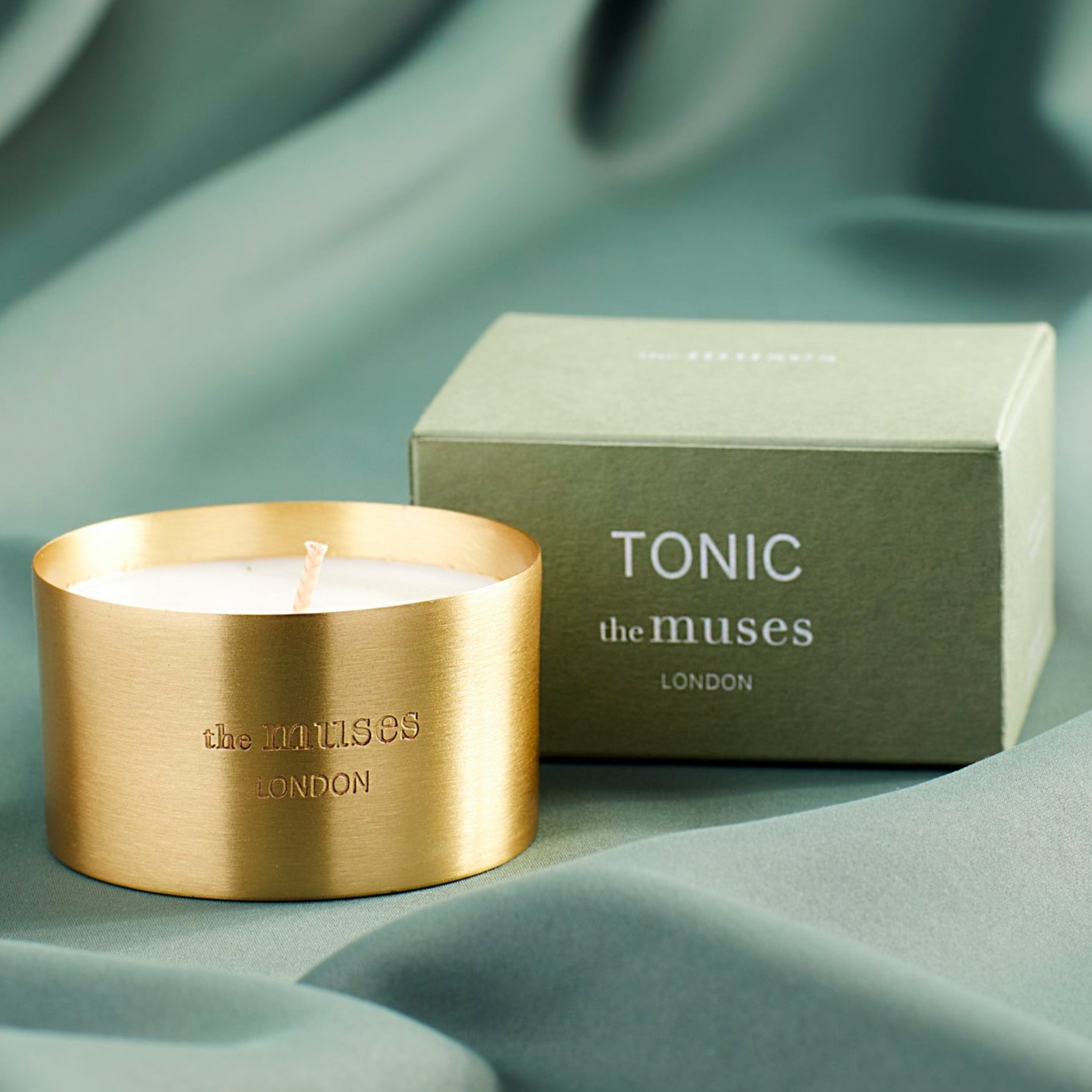 Tonic scented 100% natural wax candle 110g in pure brass container next to green candle box with closed lid. Front