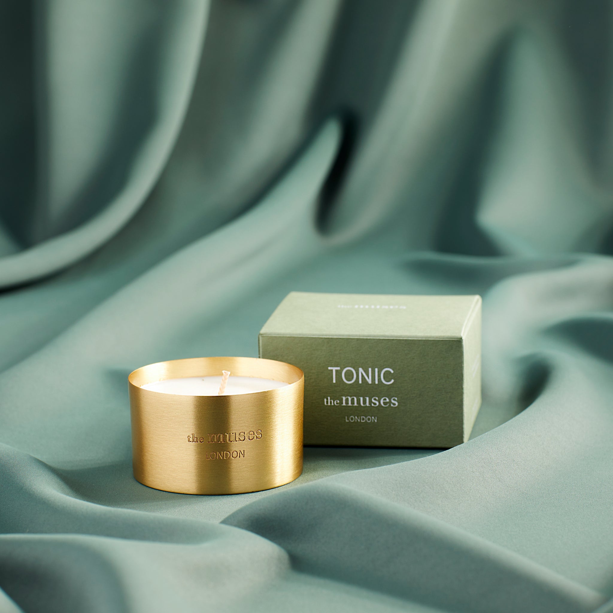 Tonic scented 100% natural wax candle 110g in pure brass container next to green candle box with closed lid. Front