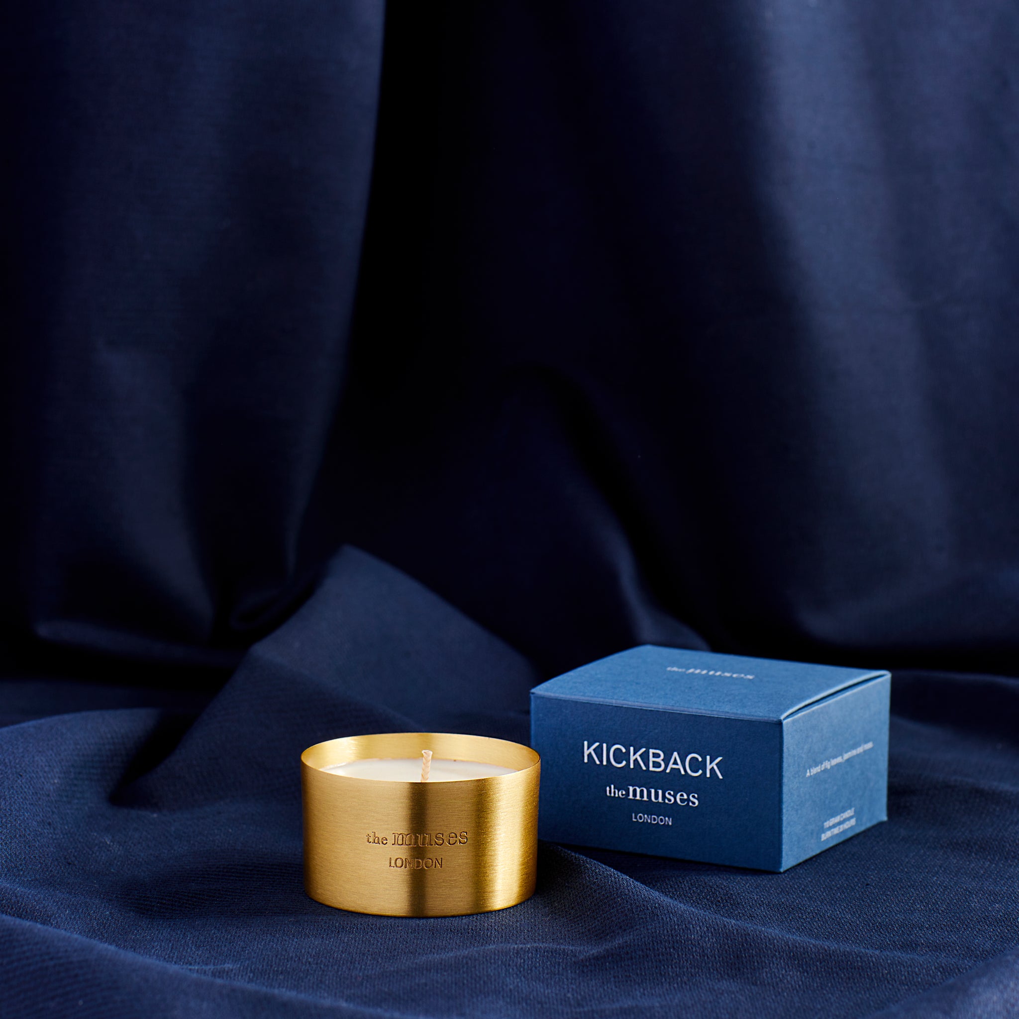 Kickback scented 100% natural wax candle 110g in pure brass container next to blue candle box with closed lid. Front