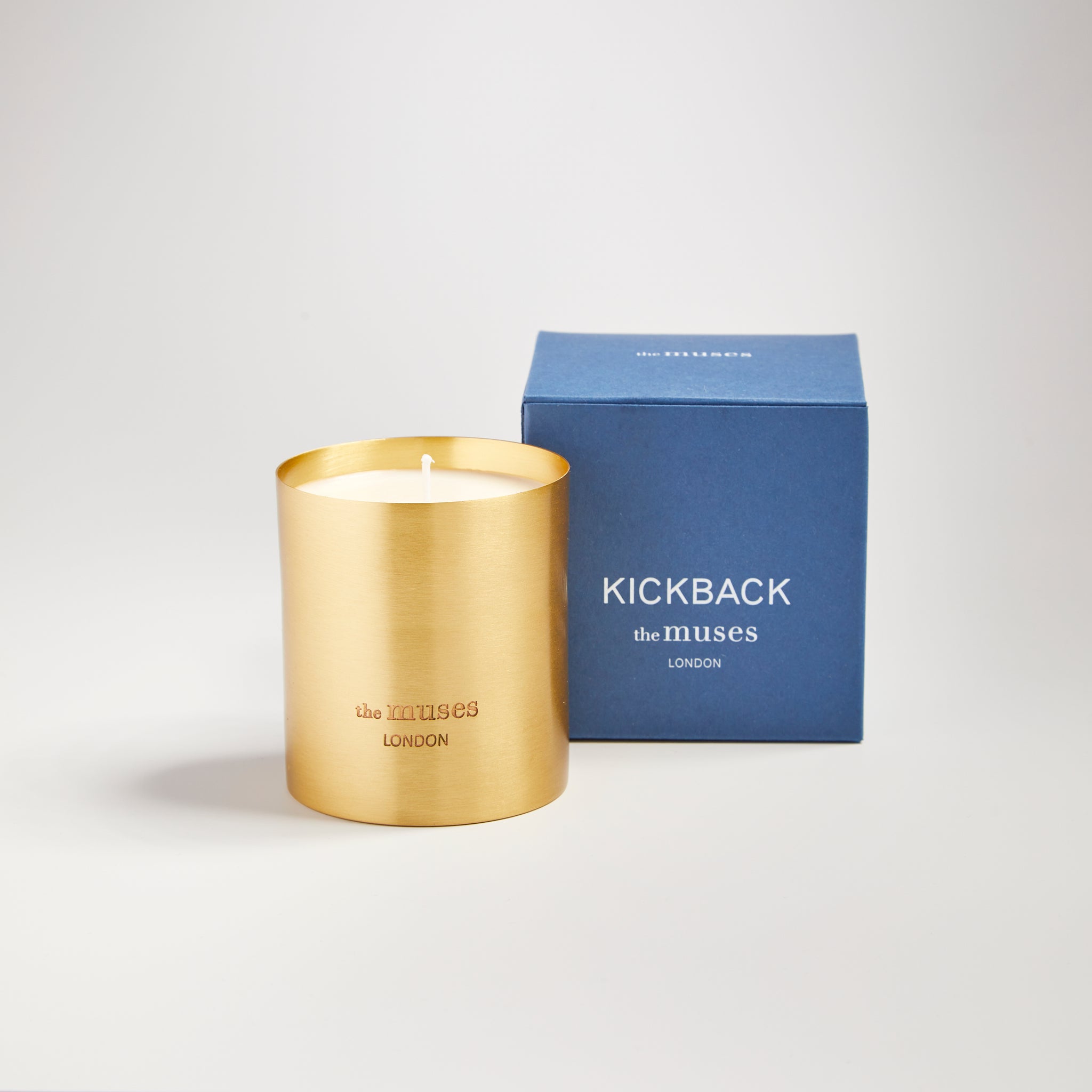 Kickback scented 100% natural wax candle 220g in pure brass container next to blue candle box with closed lid. Front