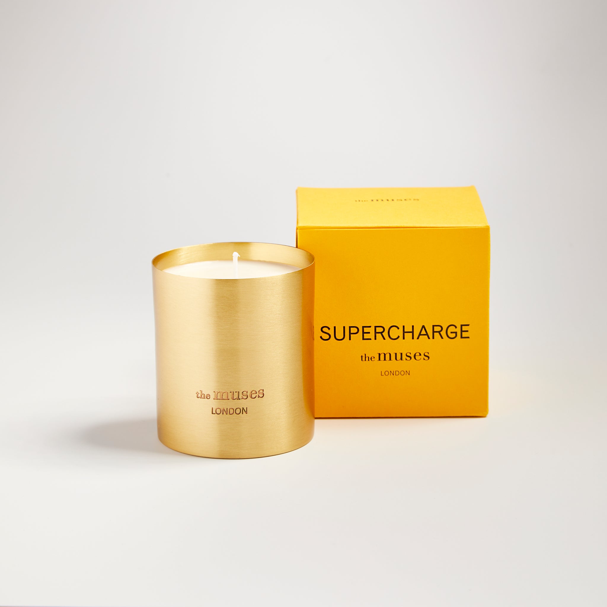Supercharge scented100% natural wax candle 220g in pure brass container next to bright yellow candle box with closed lid. Front.