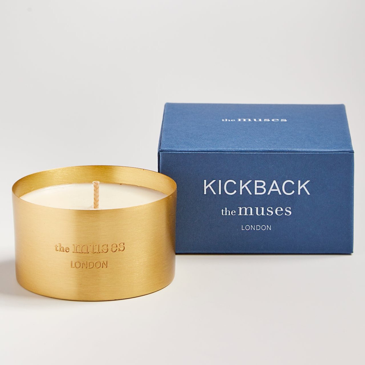 Kickback scented 100% natural wax candle 110g in pure brass container next to blue candle box with closed lid. Front