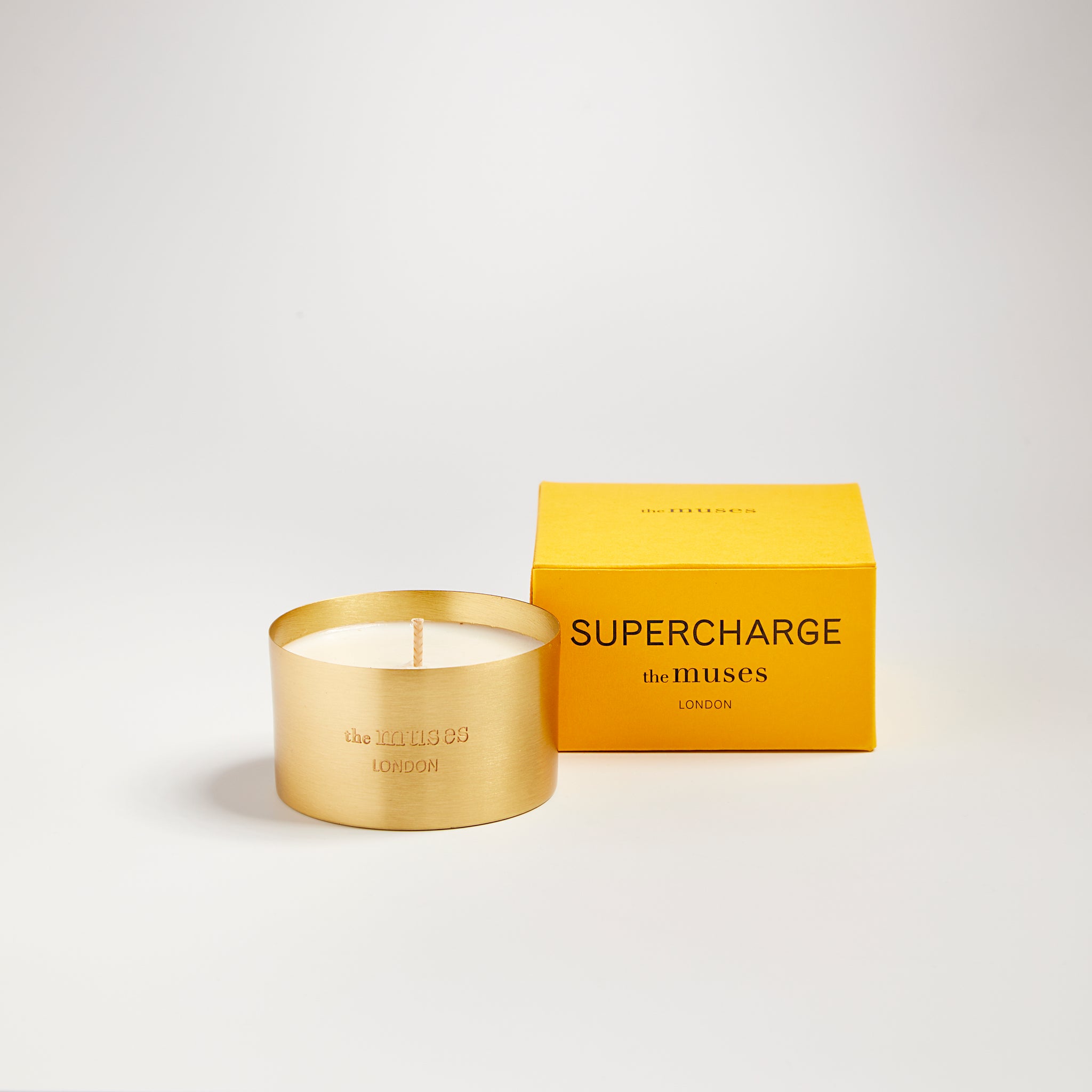 Supercharge scented100% natural wax candle 110g in pure brass container next to bright yellow candle box with closed lid. Front.