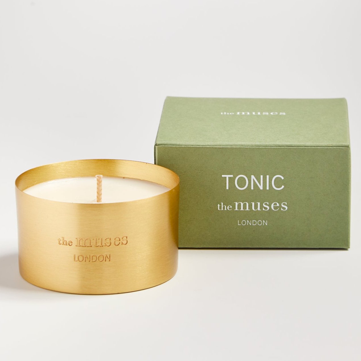 Tonic scented 100% natural wax candle 110g in pure brass container next to green candle box with closed lid. Front